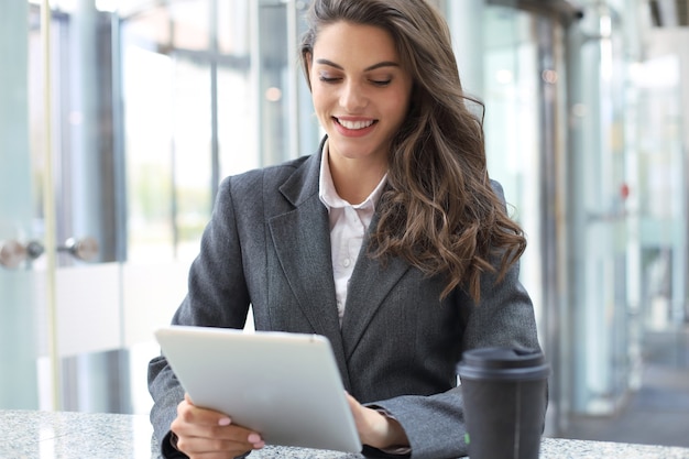 Jovem empresária sorridente no escritório trabalhando em tablet digital.