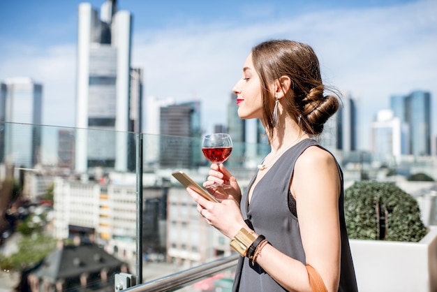 Jovem empresária tomando vinho no terraço com uma bela vista dos arranha-céus da cidade de Frankfurt