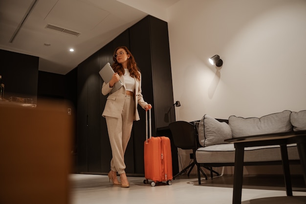 Jovem empresária trabalha no hotel. Conceito de viagem de negócios. Modelo feminino ruivo em um elegante terno e mala laranja faz o check-in no hotel.