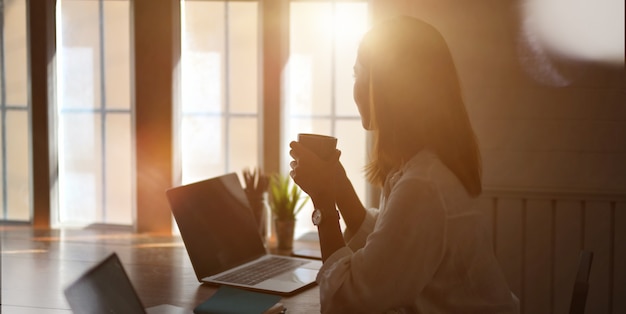 jovem empresária trabalhando com computador portátil e beber uma xícara de café