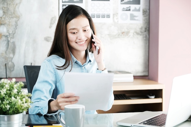 Jovem empresária trabalhando e falando telefone na mesa do escritório