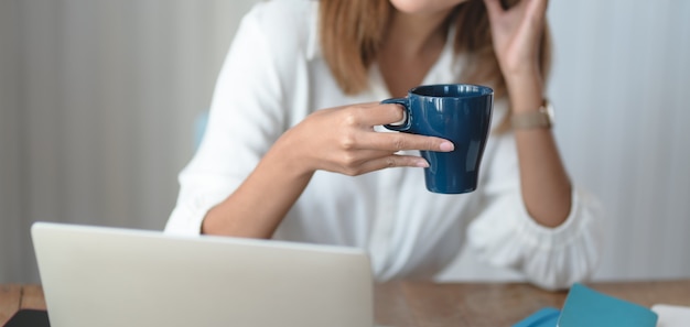 jovem empresária trabalhando em seu projeto e bebendo uma xícara de café no escritório moderno