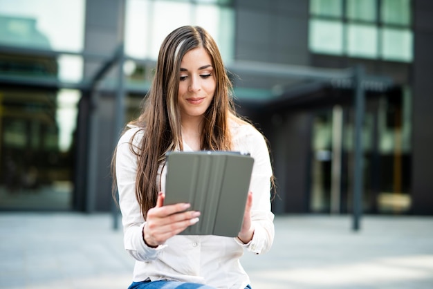 Jovem empresária usando um tablet digital ao ar livre sentada em um banco