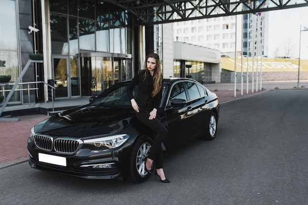 Jovem empresária vestida de preto com um carro caro