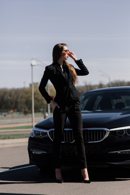 Foto jovem empresária vestida de preto com um carro caro