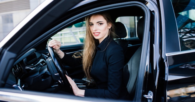 Jovem empresária vestida de preto com um carro caro