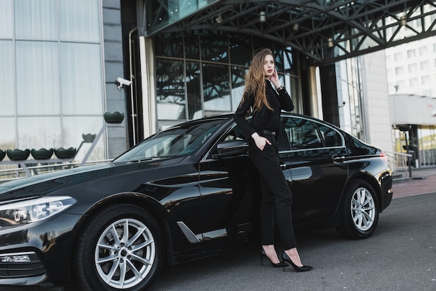 Foto jovem empresária vestida de preto com um carro caro