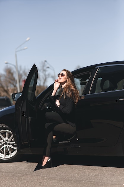 Jovem empresária vestida de preto com um carro caro