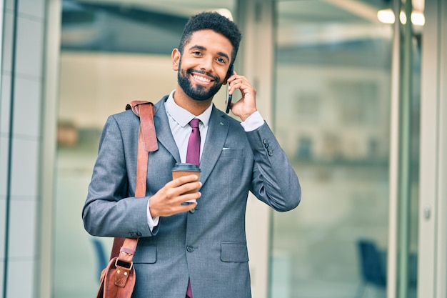 Jovem empresário afro-americano falando no smartphone e bebendo café para viagem na cidade