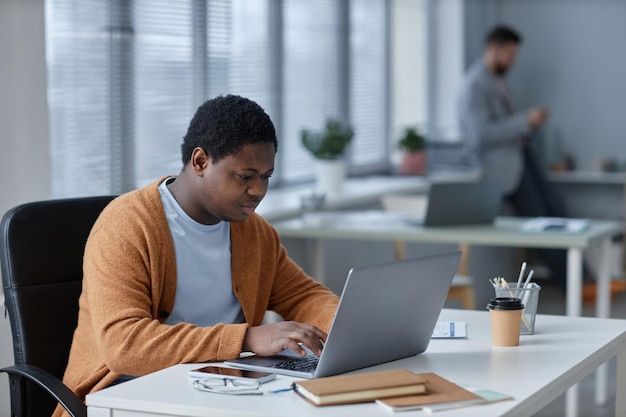 Jovem empresário afro-americano sério digitando no teclado do laptop