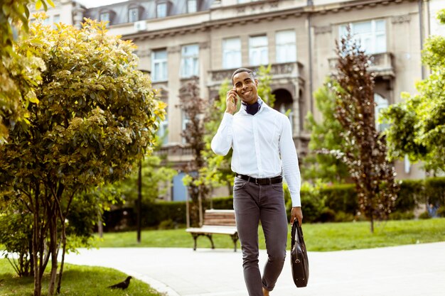 Jovem empresário afro-americano usando um telefone celular enquanto caminhava na rua aa