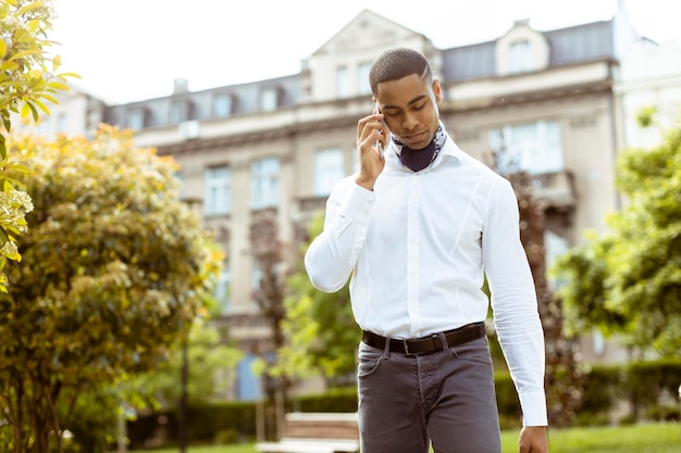 Jovem empresário afro-americano usando um telefone celular enquanto caminhava na rua aa