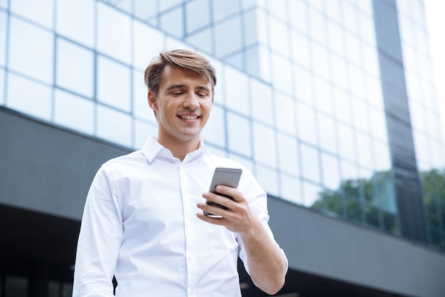 Jovem empresário alegre usando smartphone perto do centro de negócios