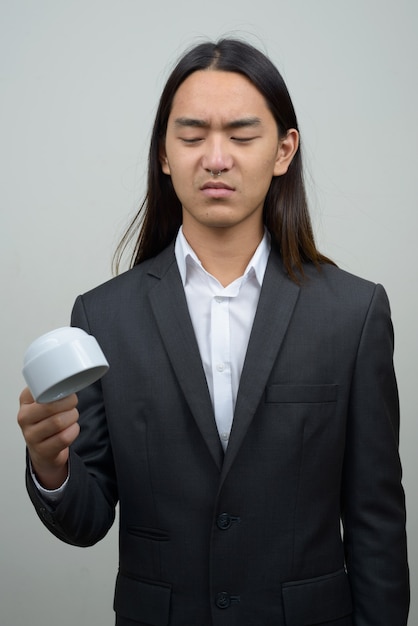 Jovem empresário asiático estressado com cabelo comprido segurando uma xícara de café de cabeça para baixo