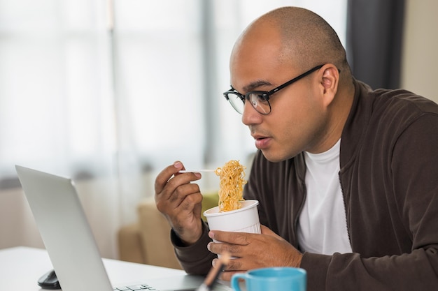 Jovem empresário asiático trabalhando com laptop autônomo indiano comendo macarrão instantâneo enquanto trabalhava