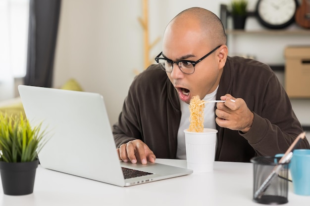 Jovem empresário asiático trabalhando com laptop autônomo indiano comendo macarrão instantâneo enquanto trabalhava