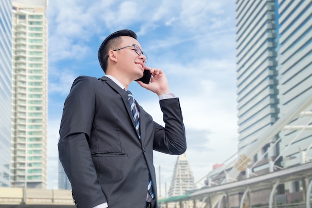 Jovem empresário asiático vestindo terno preto falando via telefone inteligente