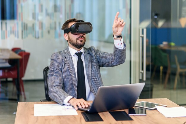 Jovem empresário barbudo caucasiano em terno azul usando óculos de proteção vr no escritório.