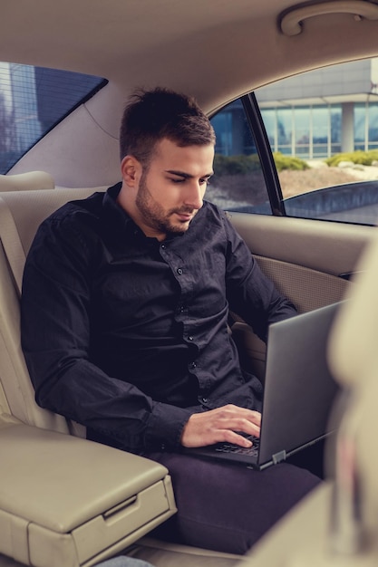 Jovem empresário barbudo com laptop no carro.