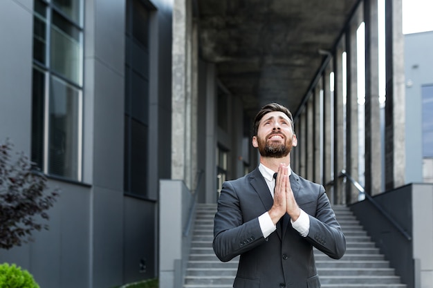 Jovem empresário barbudo do retrato implora a Deus pelo sucesso com esperança, levantando as mãos para o céu. homem de negócios pede sorte e ora por uma solução bem-sucedida. Pedindo ajuda.