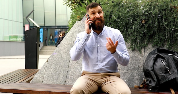 Jovem empresário barbudo falando ao telefone ao ar livre.