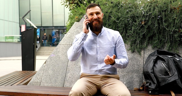 Jovem empresário barbudo falando ao telefone ao ar livre.