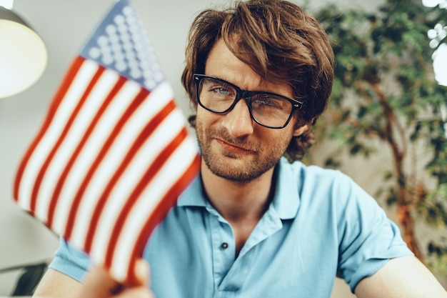 Jovem empresário barbudo sentado à mesa com o laptop e a bandeira americana