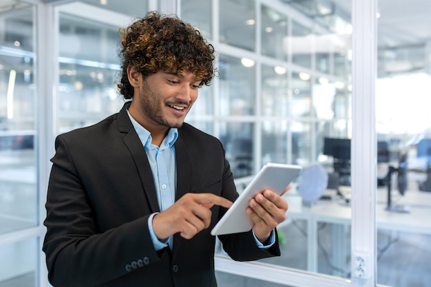 Jovem empresário bem-sucedido com computador tablet sorrindo homem hispânico trabalhando dentro de um moderno