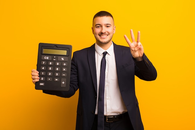 Jovem empresário bonitão contra parede plana com uma calculadora