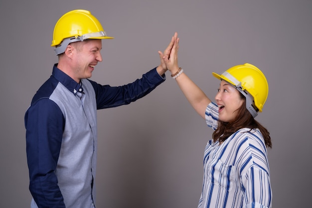 jovem empresário bonitão e madura empresária asiática usando capacete de segurança