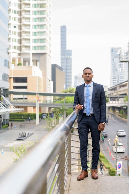 Jovem empresário bonitão em terno contra a vista de um edifício moderno ao ar livre