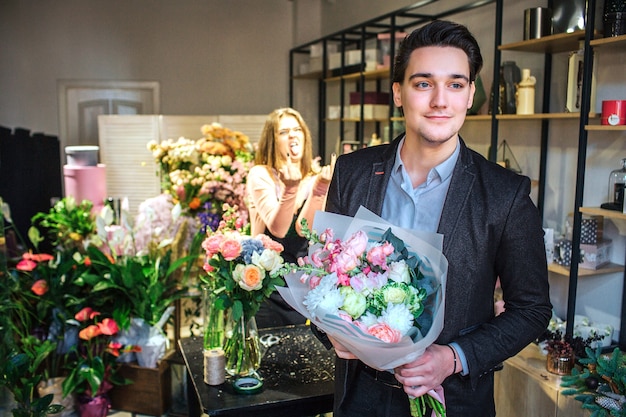 Jovem empresário bonitão fica na loja de flores. ele segura o buquê nas mãos. ele esta sozinho no quarto