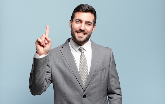 Jovem empresário bonitão sorrindo alegre e feliz, apontando para cima com uma das mãos para copiar o espaço