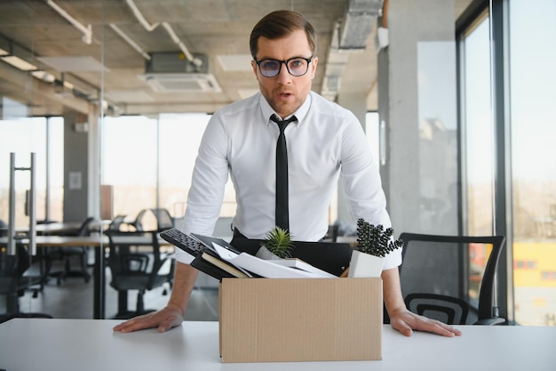 Jovem empresário bonito em escritório moderno leve com caixa de papelão Último dia de trabalho Trabalhador de escritório chateado é demitido