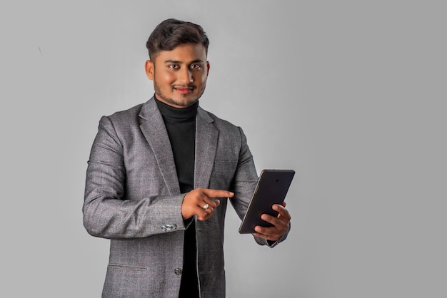 Jovem empresário bonito segurando e usando smartphone ou celular ou tablet em fundo cinza