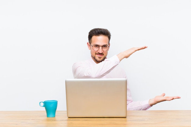 Jovem empresário bonito sorrindo, sentindo-se feliz, positivo e satisfeito, segurando ou mostrando o objeto ou conceito no espaço da cópia