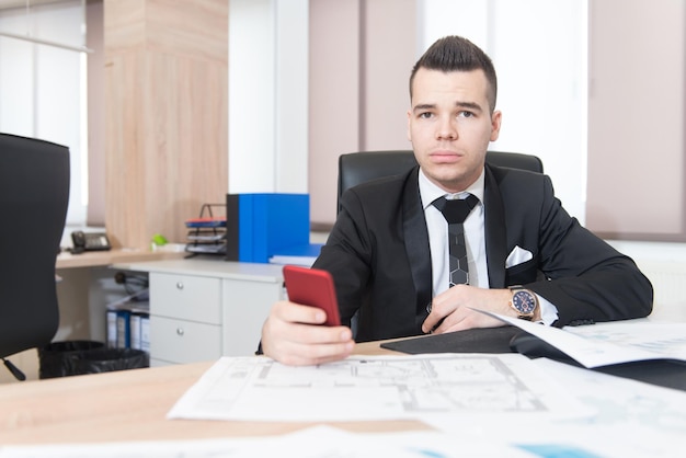 Jovem empresário bonito trabalhando na mesa no escritório moderno falando no telefone