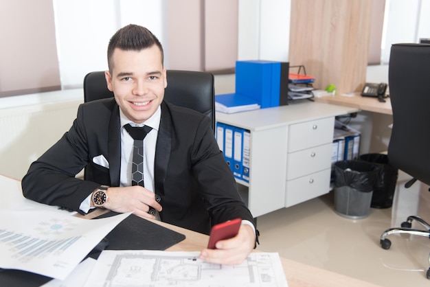 Jovem empresário bonito trabalhando na mesa no escritório moderno falando no telefone