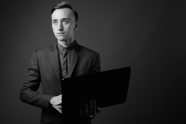 jovem empresário bonito usando laptop contra parede cinza. Preto e branco