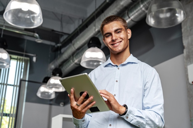 Foto jovem empresário bonito usando tablet digital enquanto está de pé no escritório