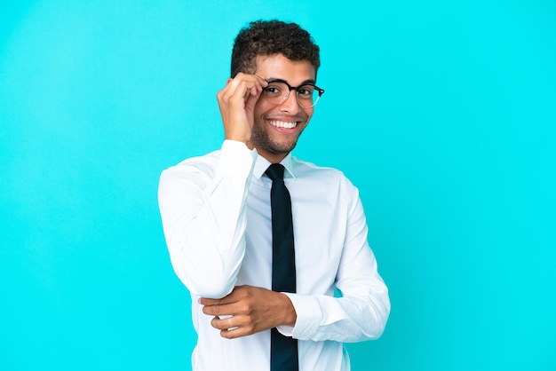 Jovem empresário brasileiro isolado em um fundo azul com óculos e feliz