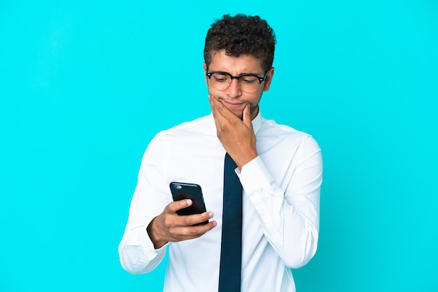 Jovem empresário brasileiro isolado em um fundo azul pensando e enviando uma mensagem