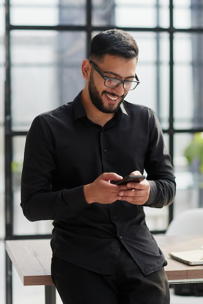 Jovem empresário casual segurando e usando o smartphone para mensagens sms