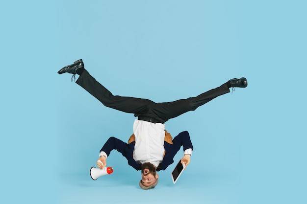 Foto jovem empresário caucasiano se divertindo, dançando a dança break no fundo azul do estúdio.