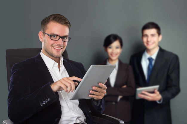 Jovem empresário caucasiano segurando um tablet pc, sua equipe na parte de trás