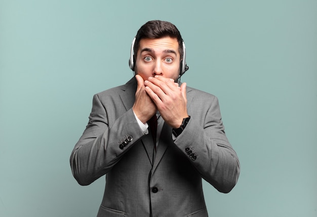 Jovem empresário cobrindo a boca com as mãos com uma expressão de choque e surpresa, mantendo um segredo ou dizendo oops conceito de telemarketing
