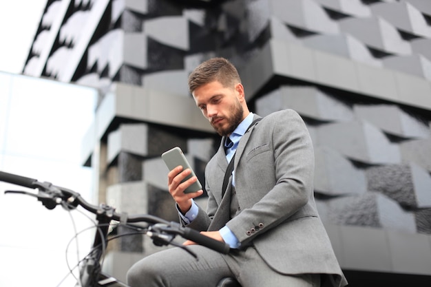 Jovem empresário com bicicleta e smartphone na rua da cidade.