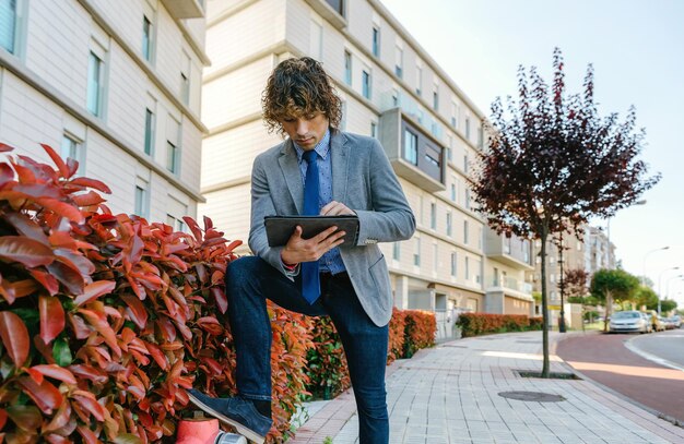 Jovem empresário com blazer e jeans trabalhando com o tablet na rua