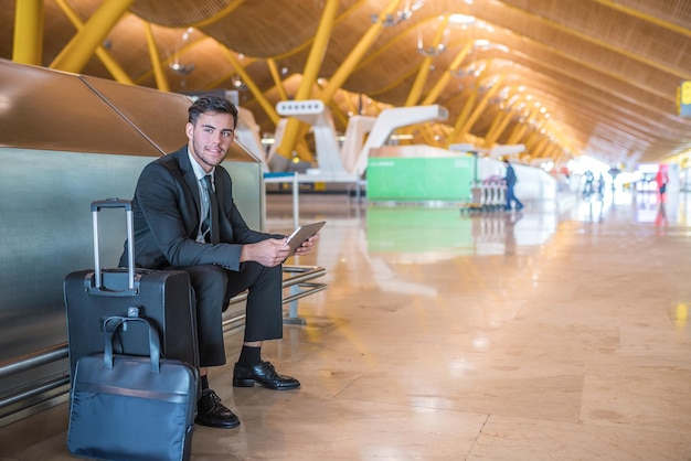 Jovem empresário com tablet sorrindo no aeroporto e esperando seu voo com bagagem