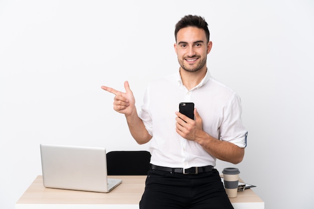 Jovem empresário com um telefone móvel em um local de trabalho, apontando o dedo para o lado